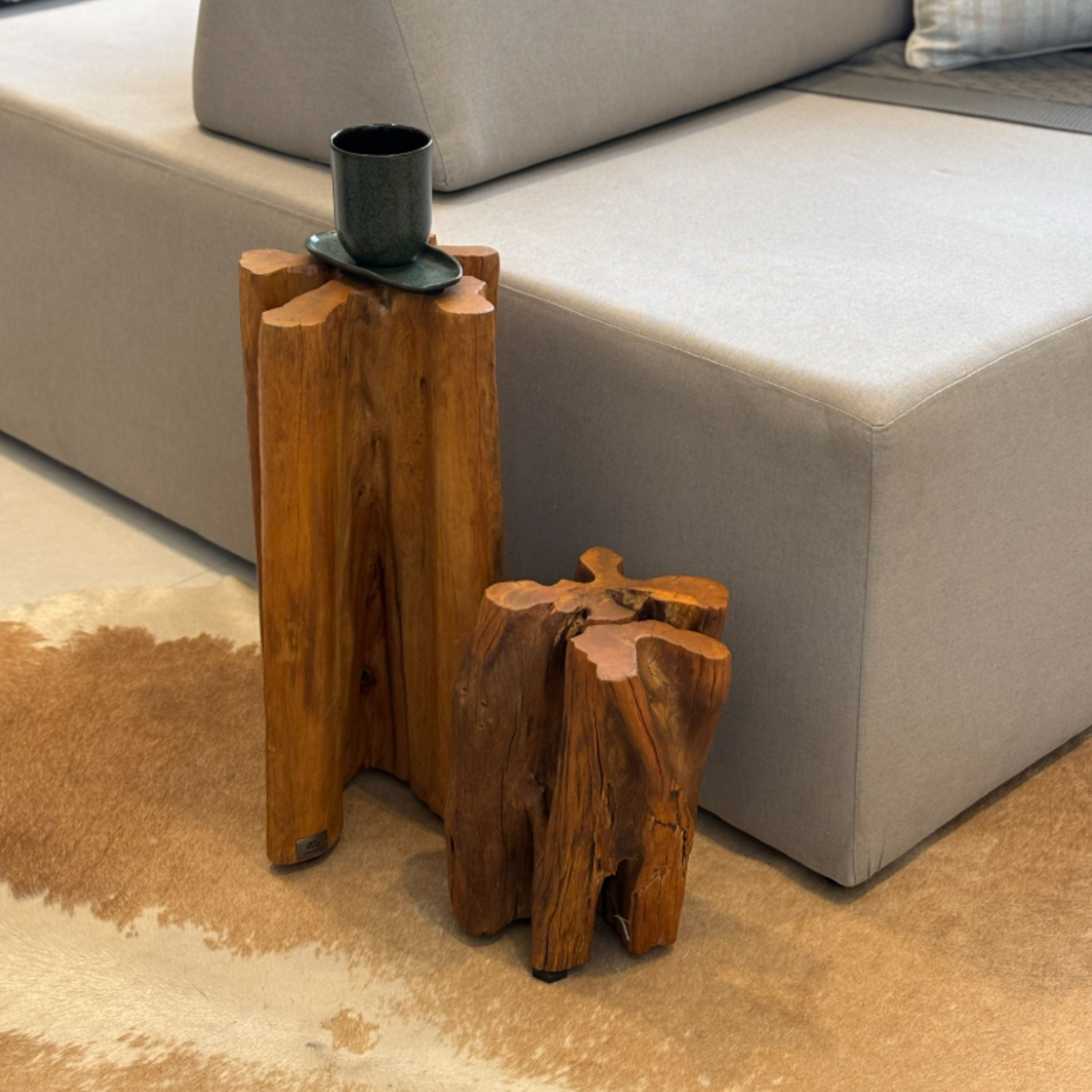 Guarantã decorativo em madeira maciça ArboREAL posicionado ao lado de sofá em ambiente contemporâneo, com função de apoio e destaque para veios naturais e forma orgânica